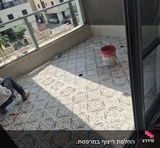 אדם עובד על רצפת מרפסת עם דלי וכלי עבודה